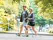 Ein älterer Mann und eine ältere Frau in Sportklamotten sind draußen im Grünen beim Nordic Walking mit Stöcken