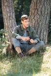 Man wearing Juzo Adventure sits in the grass in front of a tree and cuts an apple.